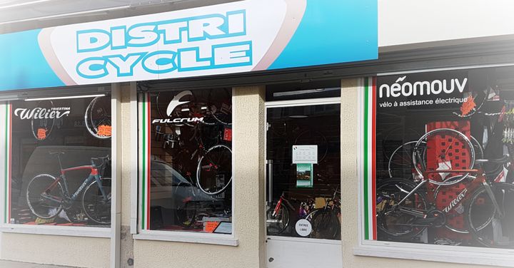 La devanture de Distri Cycle, l'enseigne bleu ciel, les vitrines Wilier, Fulcrum et Néomouv, montants vert, blanc, rouge